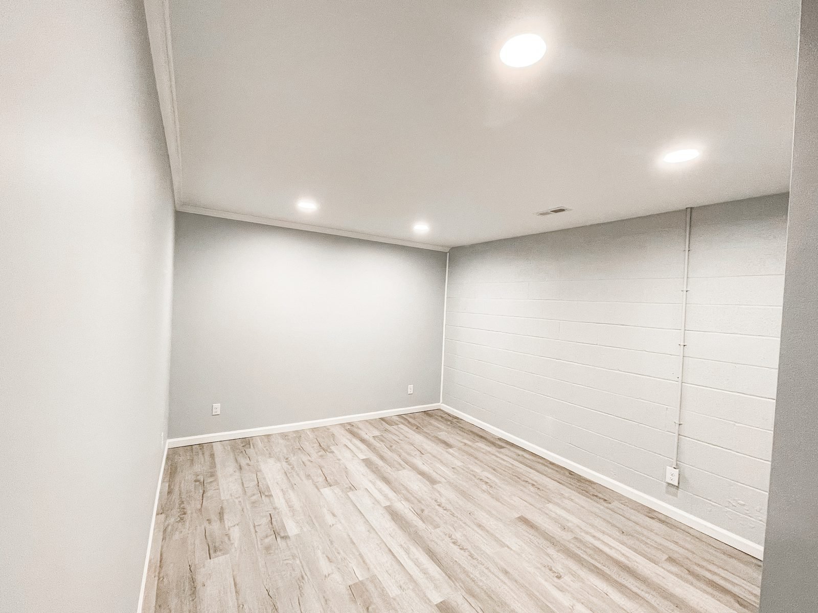 Finished basement room in Cookeville with recessed lights, gray painted drywall, a painted block wall and light vinyl plank floors by H&H Construction
